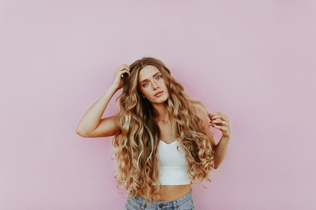 Woman with long wavy hair standing against a pink wall